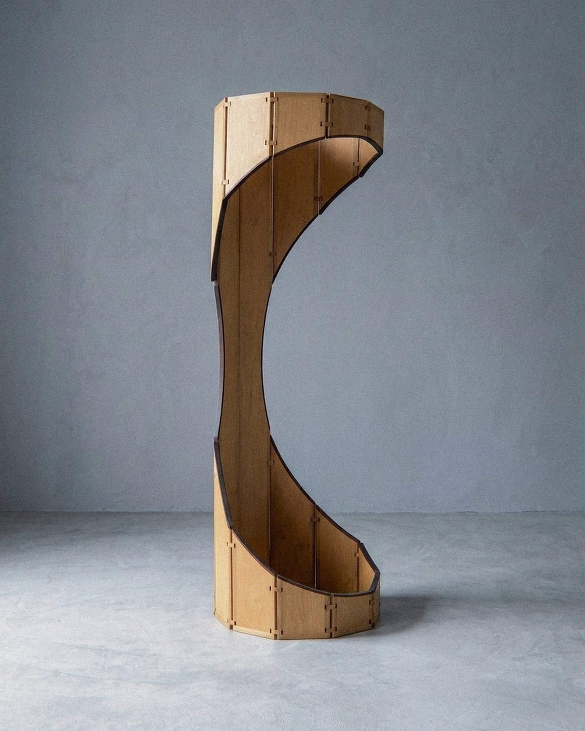 A escultura móvel Ó disposta em forma curva oca com corte lateral aberto sobre piso cinza.