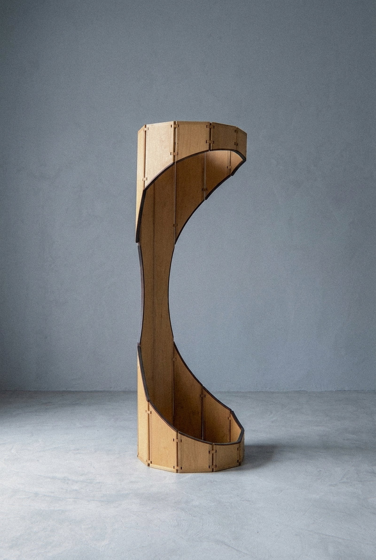 A escultura móvel Ó disposta em forma curva oca com corte lateral aberto sobre piso cinza.