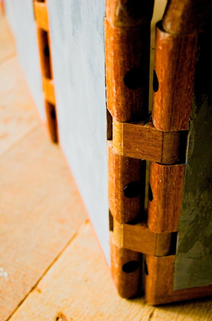 Close de uma dobradiça de madeira articulada com pinos escuros na borda da escultura móvel Fêmea.