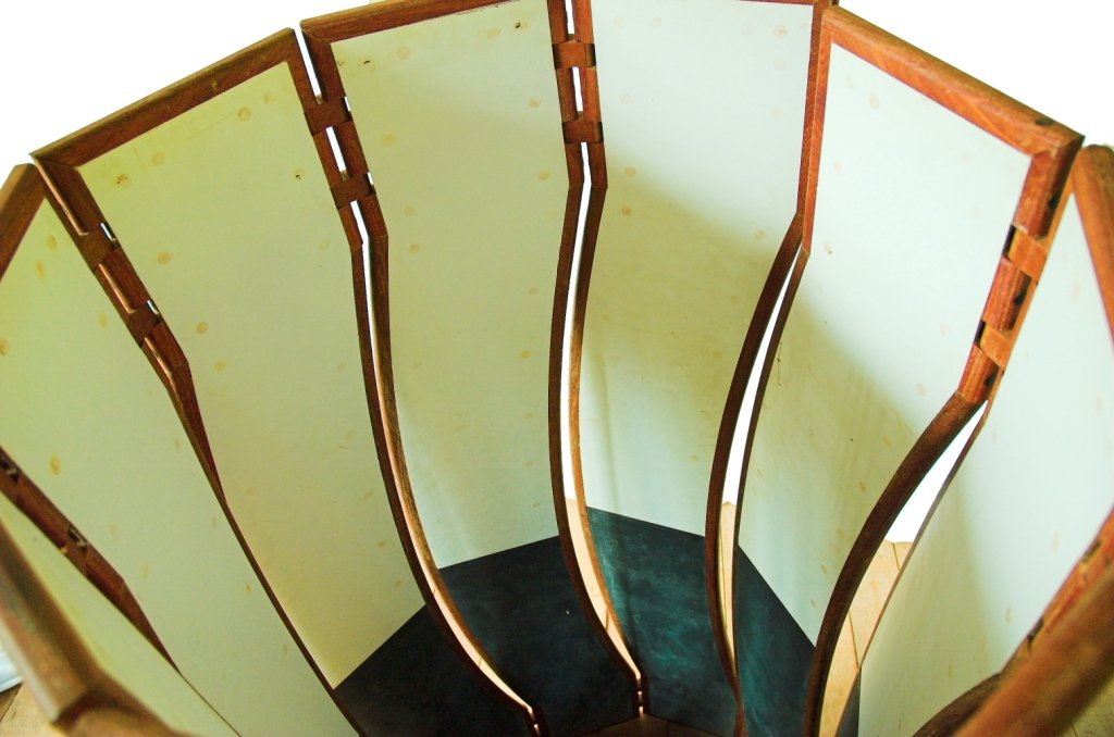 Vista superior da escultura móvel Fêmea disposta em semicírculo aberto com interior branco e base escura.