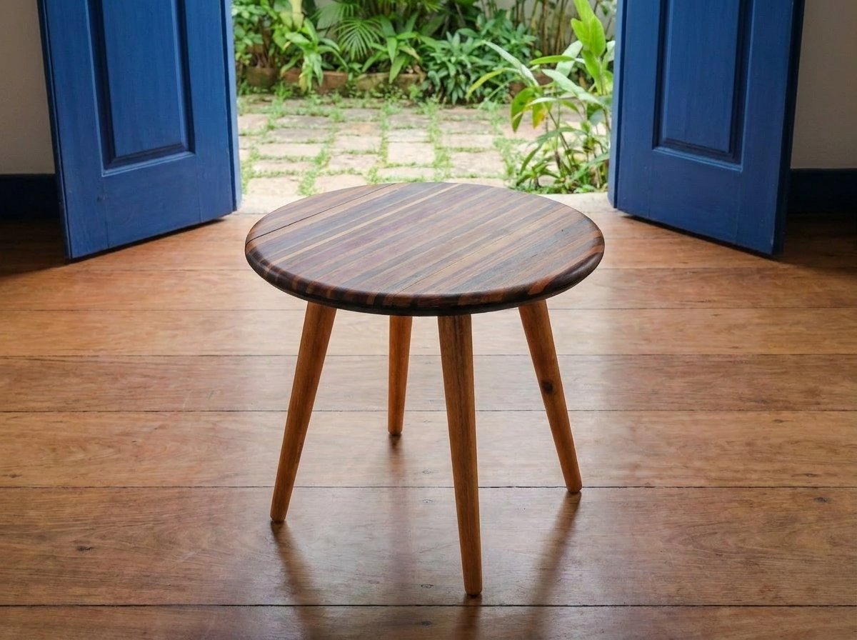 Mesa Flor em ângulo oblíquo sobre piso de madeira diante de grandes portas azuis abertas.