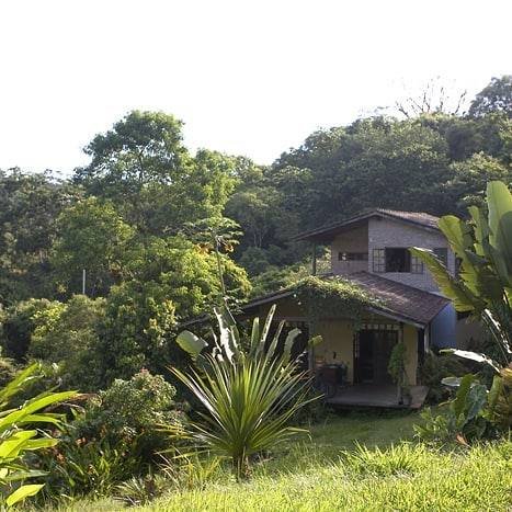 Two story house surrounded by trees on a mountain slope seen across grass.