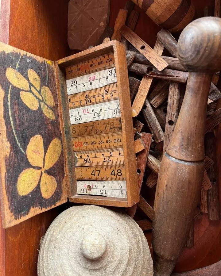 Open drawer with small wooden scraps, a small box with folding rulers, and turned wooden parts.