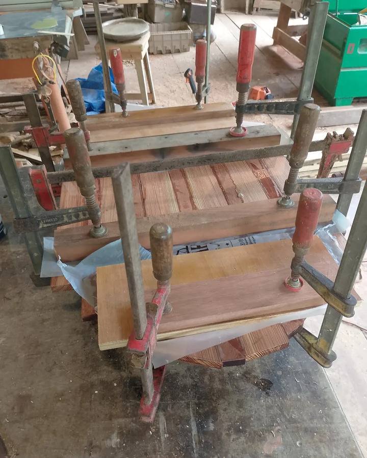 Wooden slats pressed together with metal clamps on a workshop table.