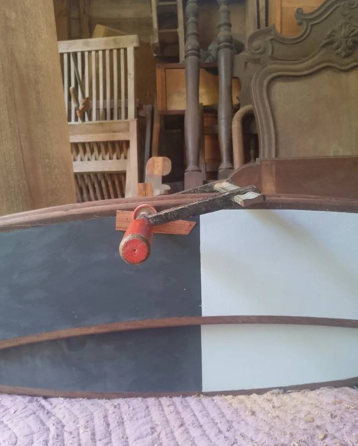 Curved wooden piece with a black and white surface held by a clamp.