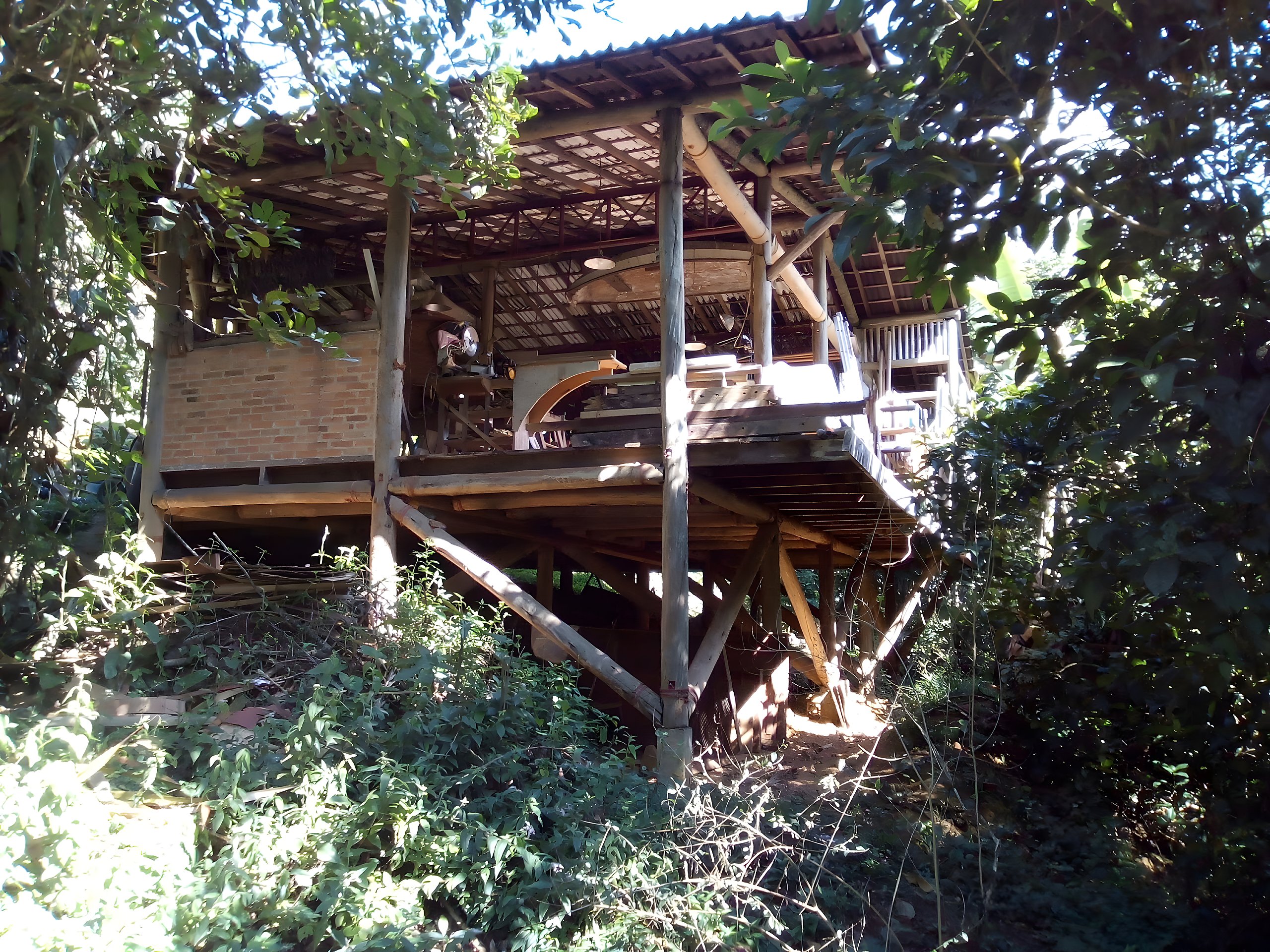 Timber workshop raised on stilts surrounded by mountain forest under natural daylight.