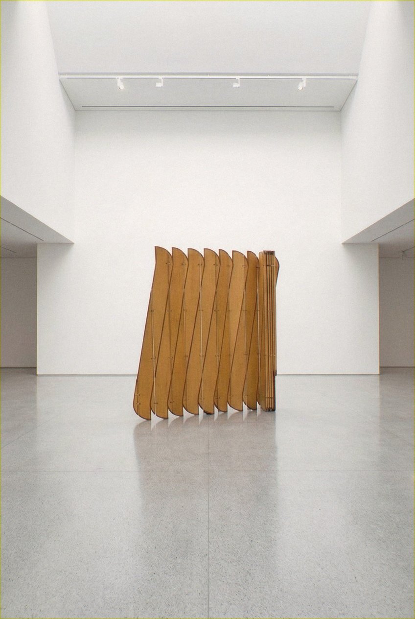 A escultura móvel Onda em compensado de maple e freixo maciço repousa no centro de um amplo átrio branco sob claraboia.