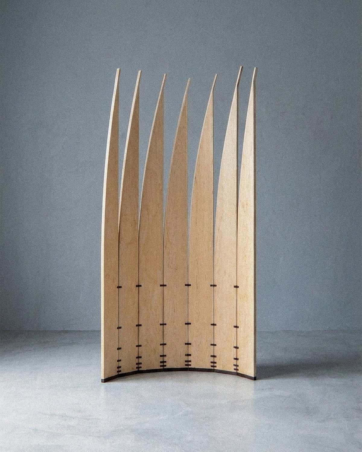 A escultura móvel Velas vista inteira à distância, disposta em arco aberto de lâminas claras sobre chão cinza.