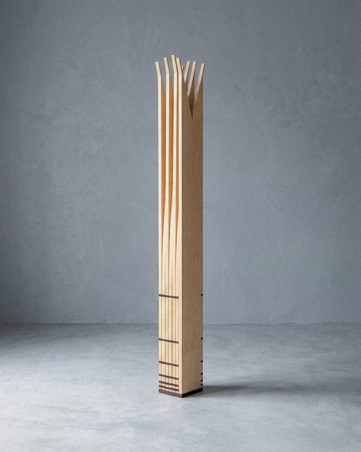 A escultura móvel Velas vista inteira e fechada como monólito colunar estreito sobre piso cinza claro.