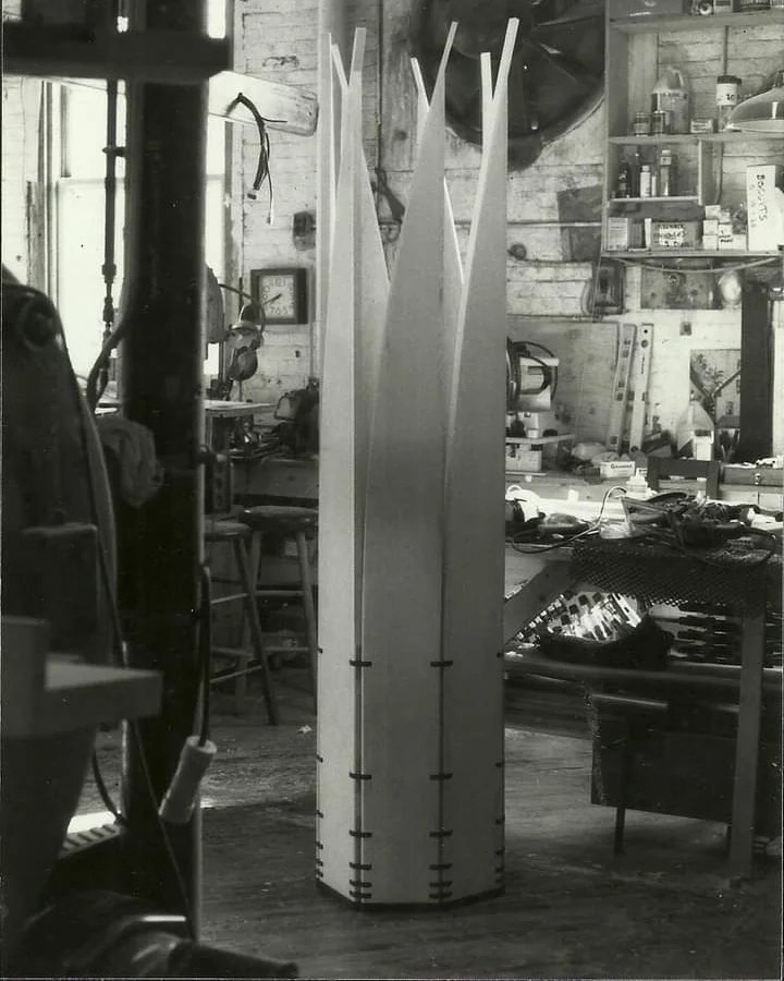 A escultura móvel Velas, fechada em forma cilíndrica, fica no chão de uma oficina de marcenaria.
